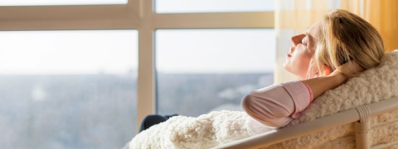 Frau liegt im Sessel entspannt und genießt die Sonne im Fenster